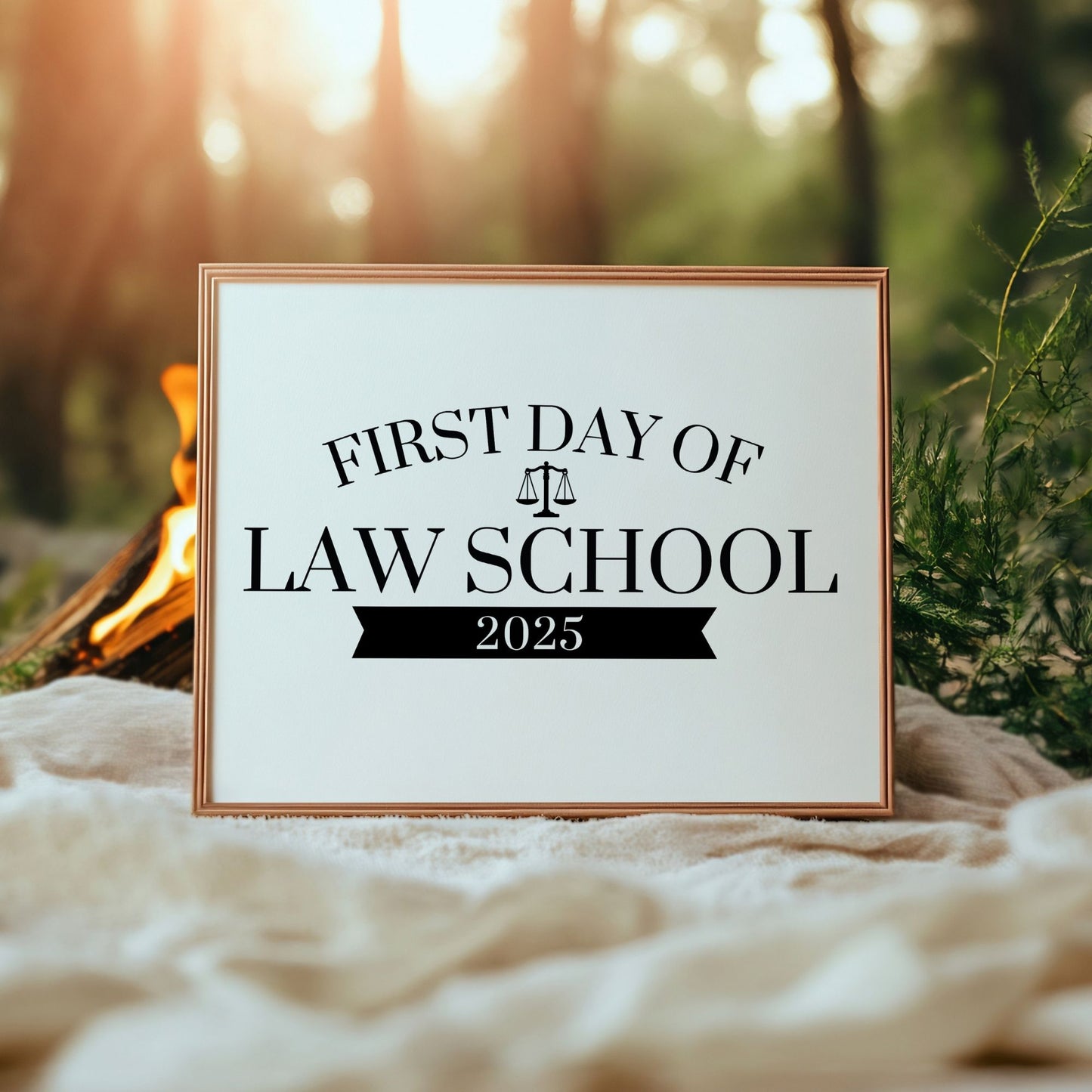 Framed sign with 'First Day of Law School 2025' text against a natural background with a campfire.