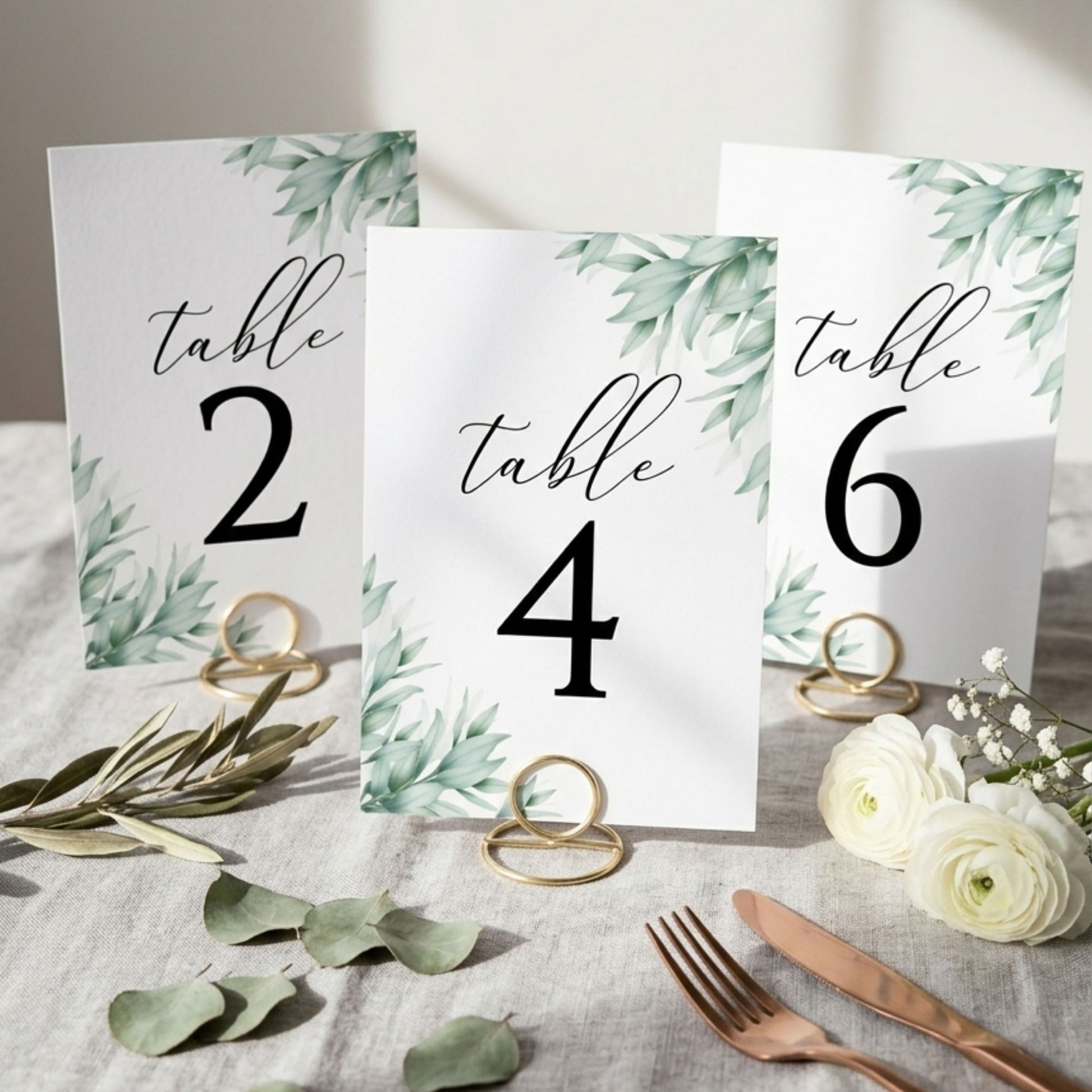 Table number cards with floral design on a table setting with silverware and flowers.