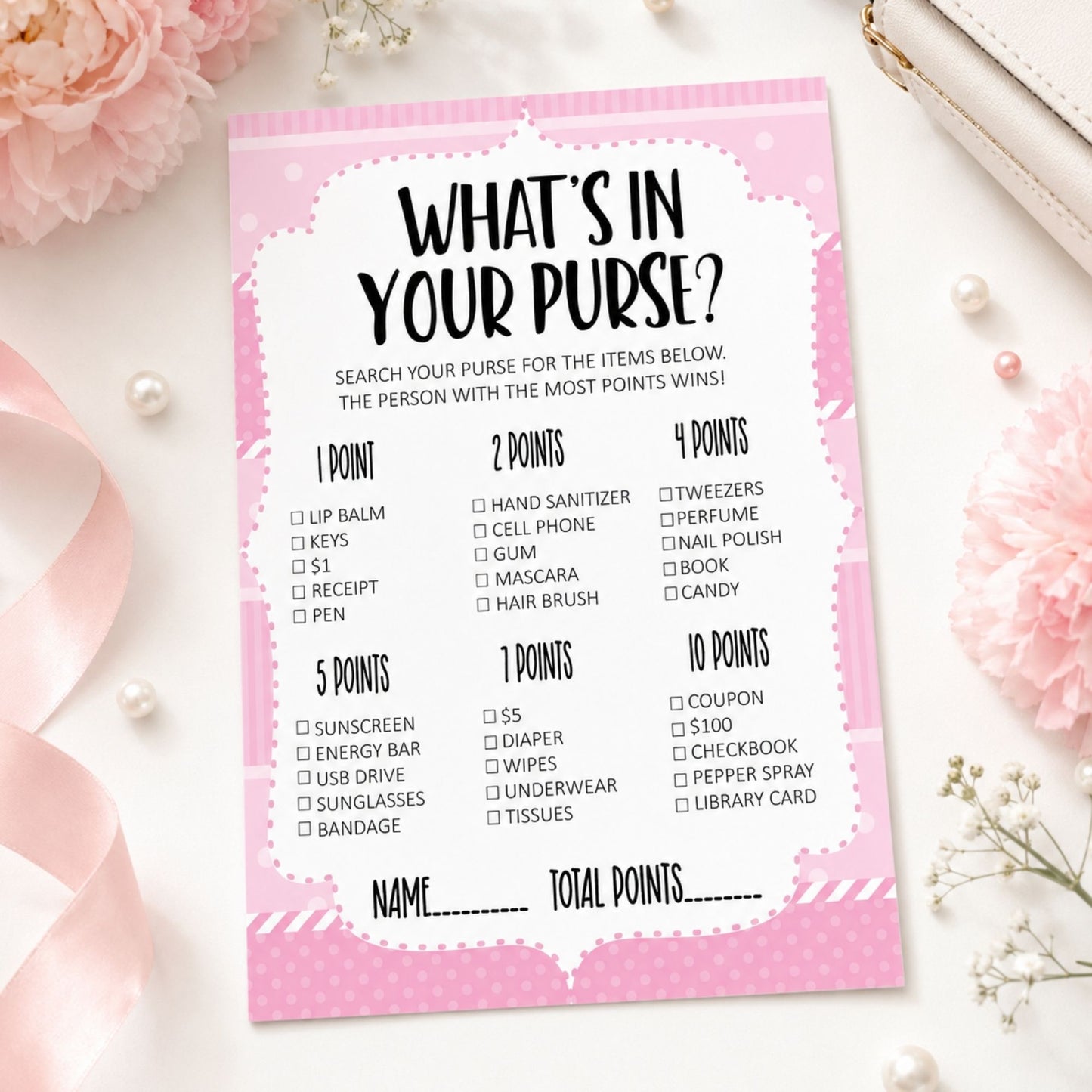 A pink and white 'What's in Your Purse?' party game score card styled in a flat-lay with pink flowers, pearls, and a white leather strap.