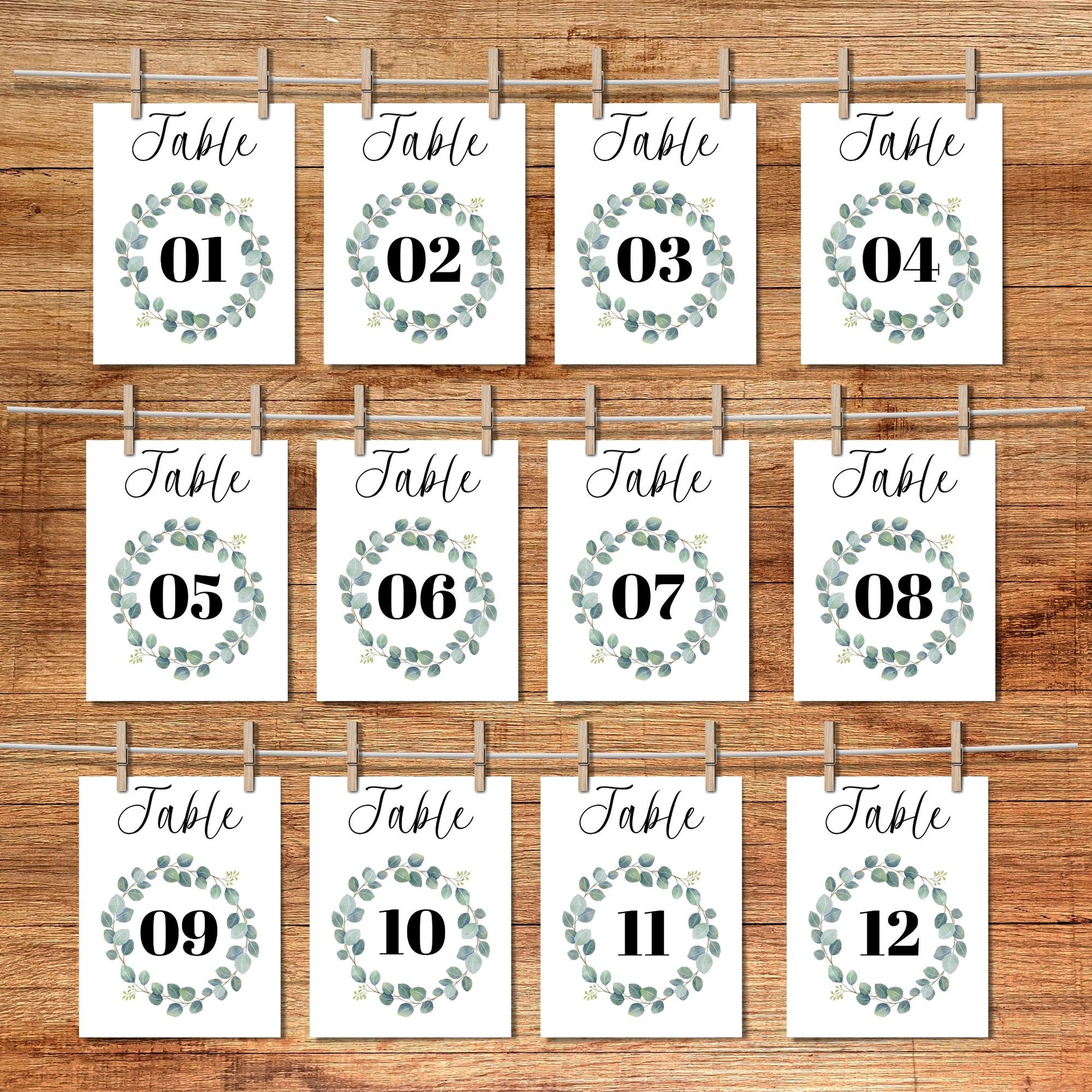 Set of 12 table number cards with green wreath designs on a wooden background