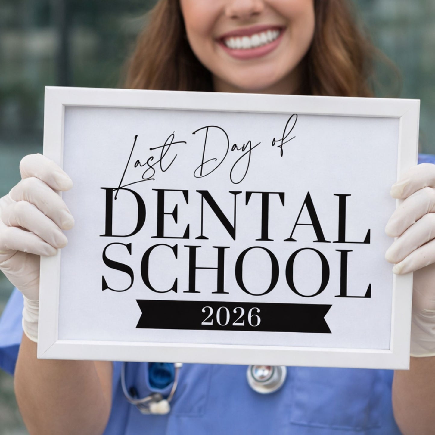 Person holding a sign for the 'Last Day of Dental School 2026' with dental scrubs and gloves.