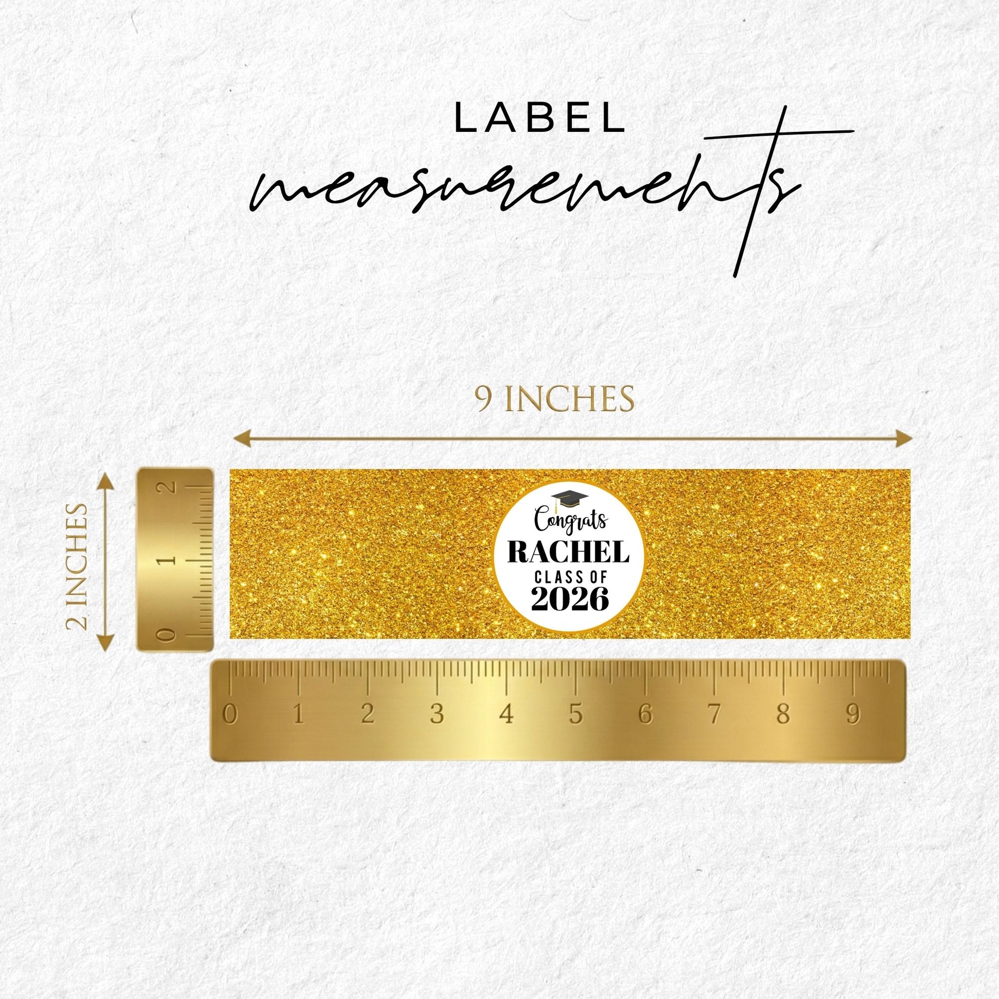 Gold label with 'Graduate Rachel Class of 2026' text on a white background with a ruler for measurement.