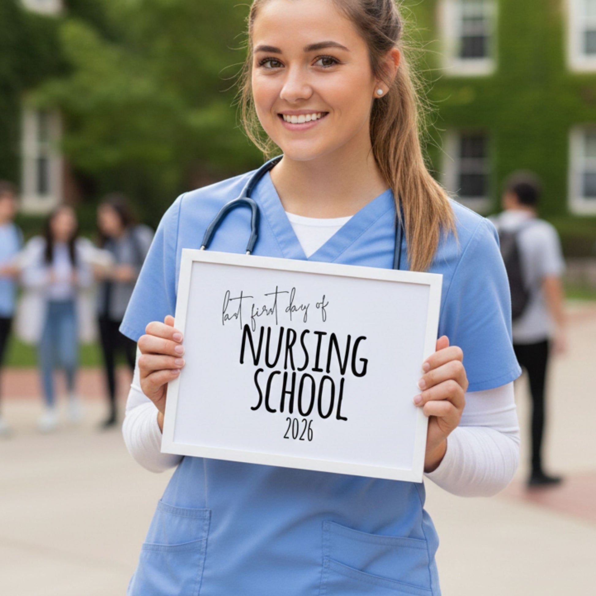 A female nursing student in blue scrubs and a stethoscope smiling on a college campus, holding a white-framed sign that says 'Last First Day of Nursing School 2026'
