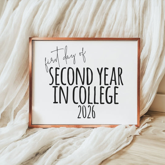 Framed sign with 'first day of second year in college 2026' text on a soft fabric background