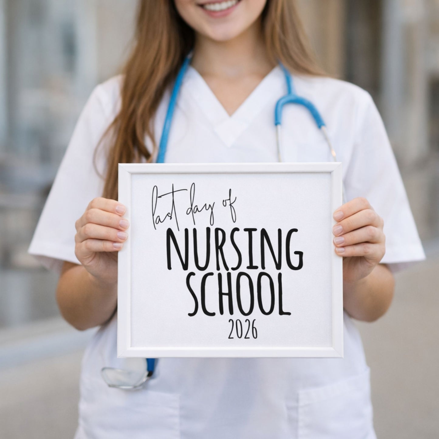 Nursing student in scrubs holding a framed Last Day of Nursing School 2026 sign. Real-world scale shot for graduation pinning ceremonies.