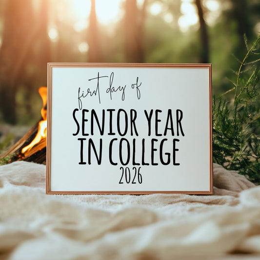 Sign with 'first day of senior year in college 2026' text in a forest setting with a campfire.