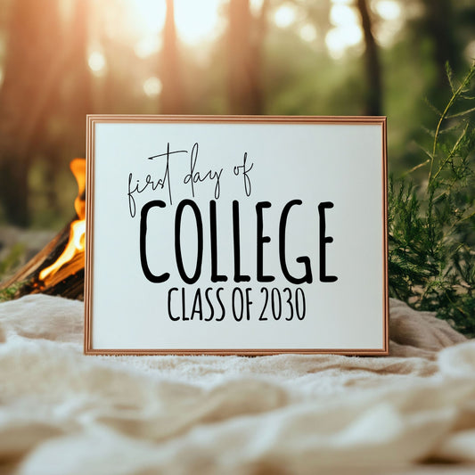 Framed sign with 'first day of college Class of 2030' text in a natural setting with a campfire.