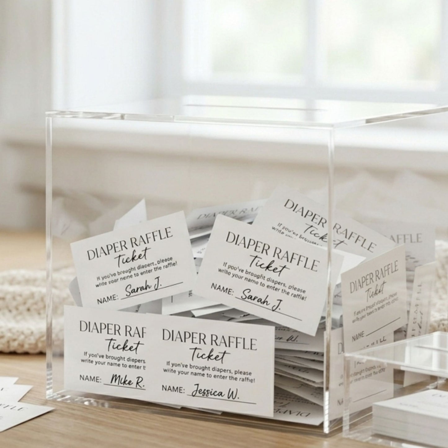 Clear acrylic box with diaper raffle tickets on a wooden surface.