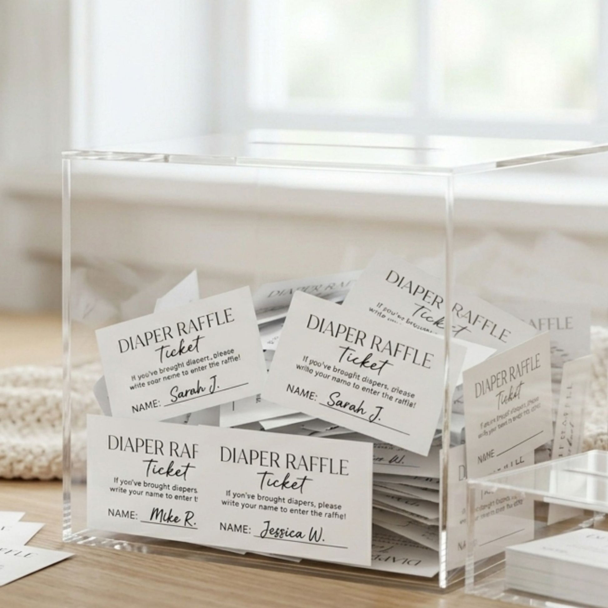 Clear acrylic box with diaper raffle tickets on a wooden surface.