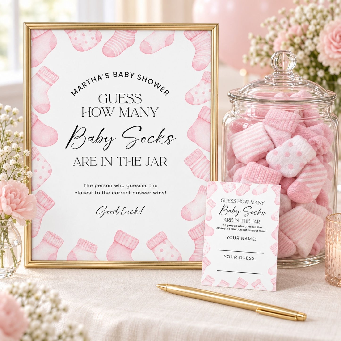 A baby shower game sign reading 'Guess How Many Baby Socks Are in the Jar' with a pink sock pattern and gold frame, displayed next to a glass jar filled with pink baby socks and a matching small entry card on a table with flowers and a pen.