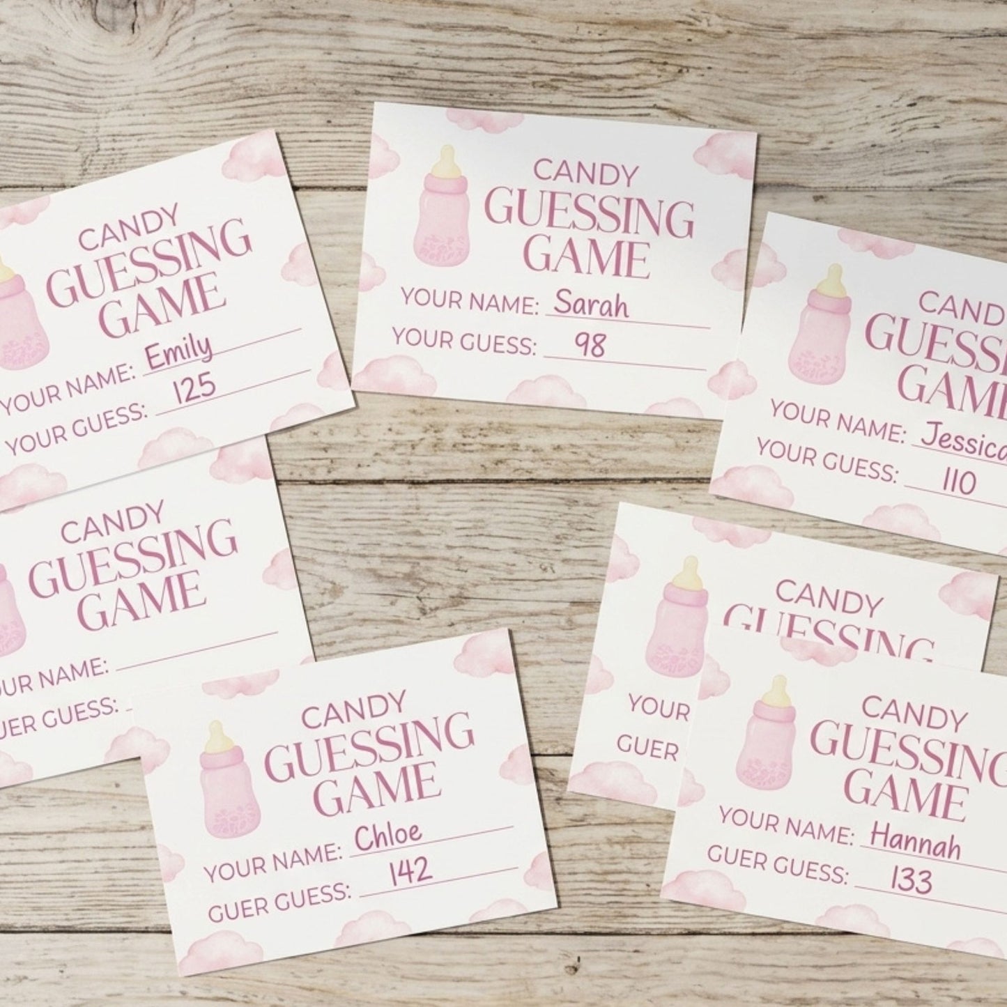 Six baby shower guessing game cards arranged on a light wood background. The cards are white with pink watercolor baby bottles, pink clouds, and pink text reading 'CANDY GUESSING GAME' along with fields for name, guess, and score.