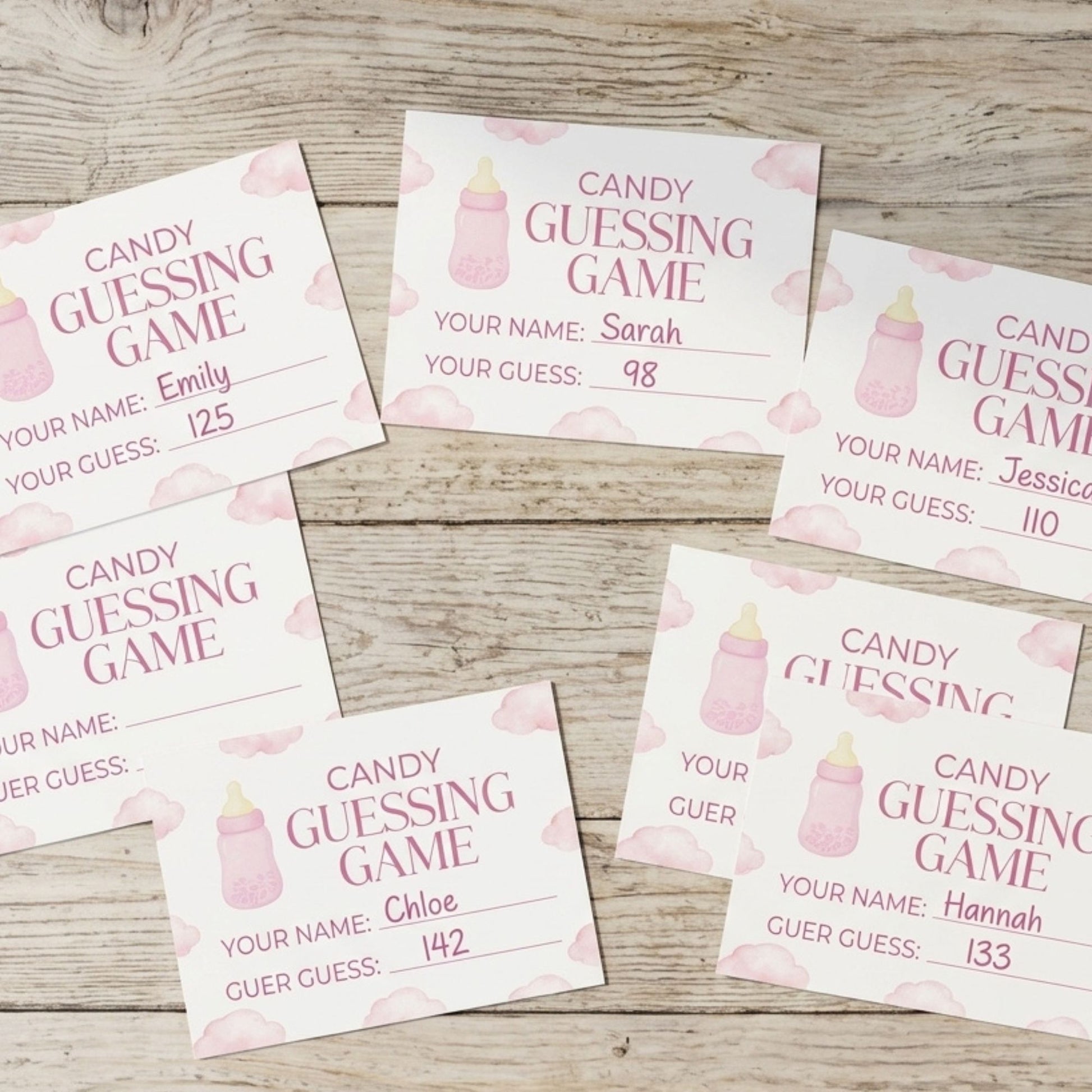 Six baby shower guessing game cards arranged on a light wood background. The cards are white with pink watercolor baby bottles, pink clouds, and pink text reading 'CANDY GUESSING GAME' along with fields for name, guess, and score.