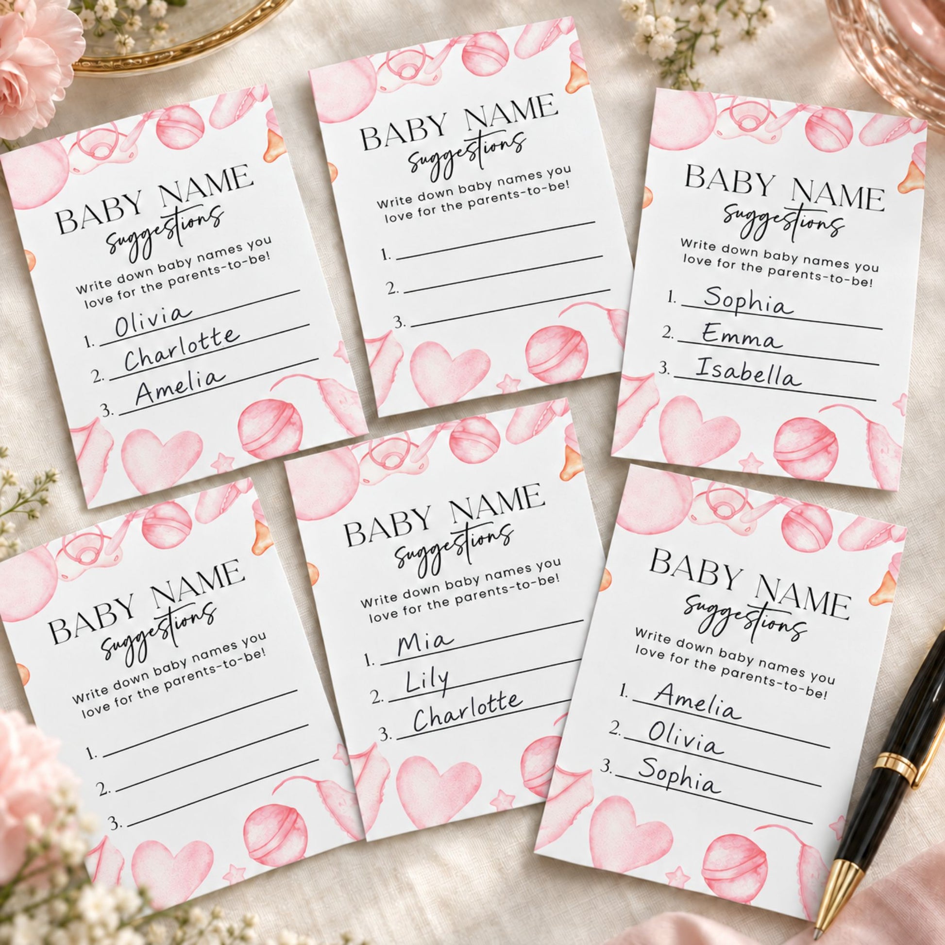 Six printed baby name suggestion cards arranged on a light fabric background with pink flowers and a black pen. The cards are white with pink watercolor hearts and the title 'BABY NAME suggestions' in black text.