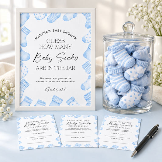 Baby shower game set featuring a white framed sign with blue baby sock illustrations, a glass jar filled with blue and white striped baby socks, and three matching participation cards on a light surface with floral props.