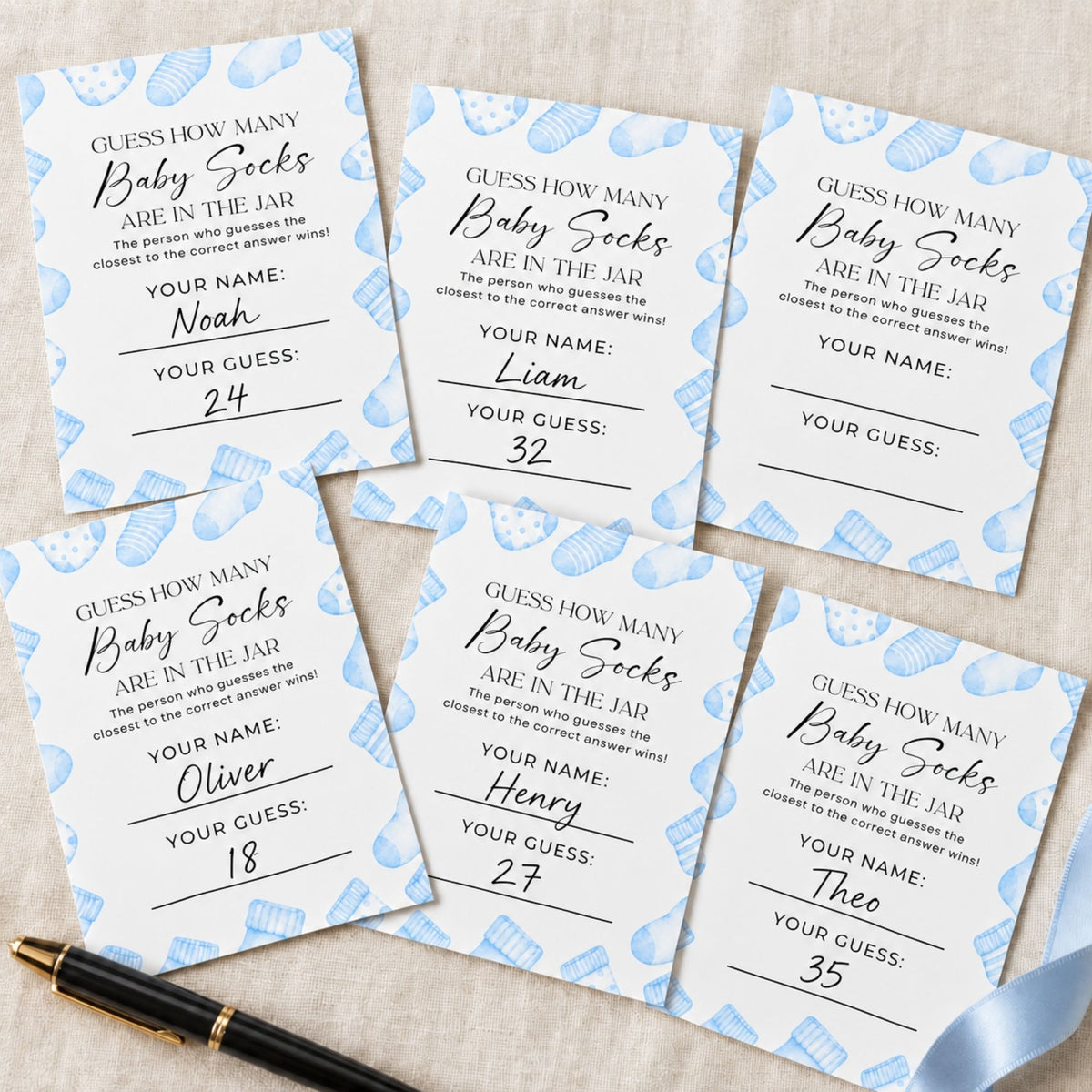 Six baby shower game cards titled 'Guess How Many Baby Socks Are in the Jar' arranged on a light beige fabric background, with a black pen placed at the bottom left.