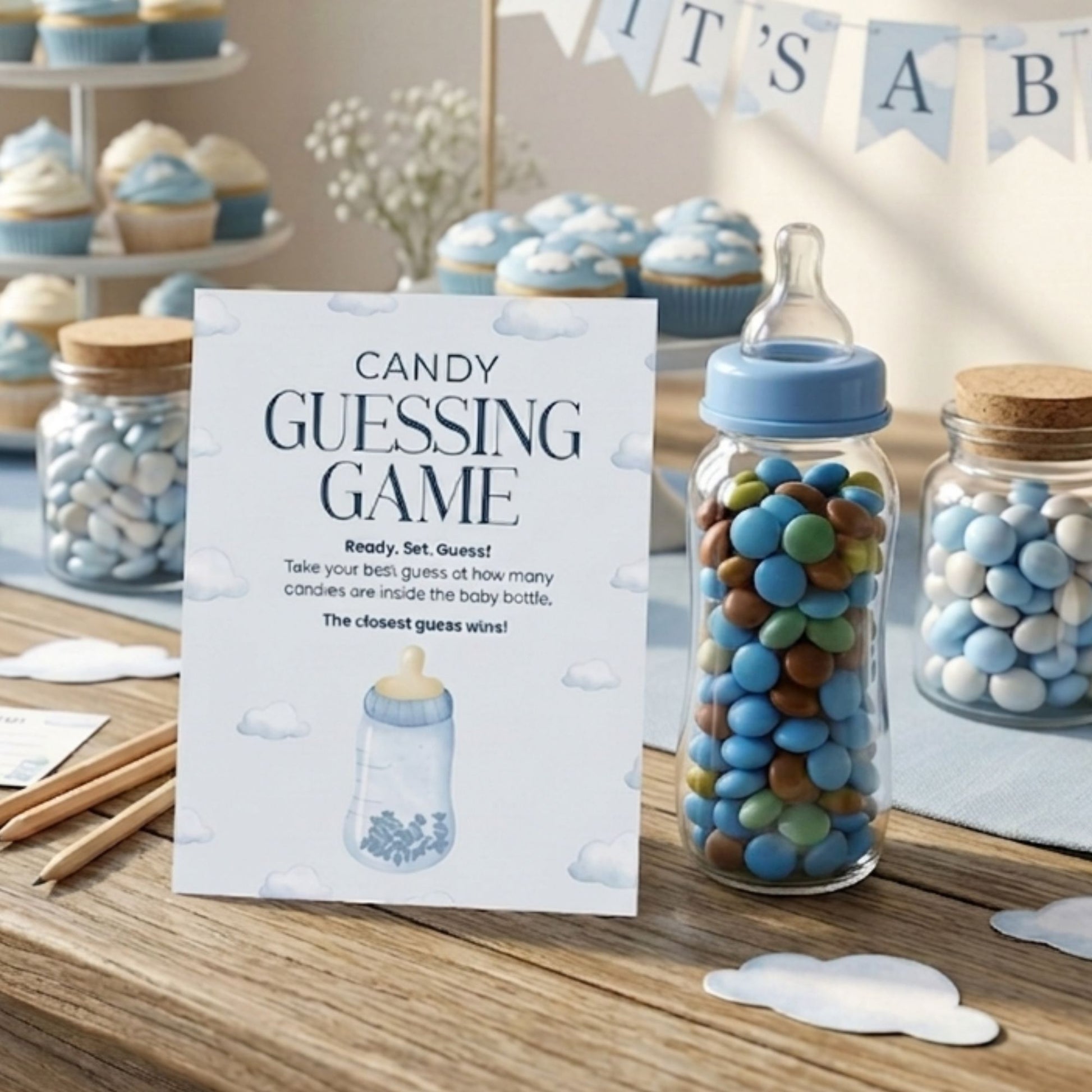 Baby boy shower candy guessing game printable sign displayed with blue and white cupcakes, baby bottle candy jar, and matching game cards for party table setup.