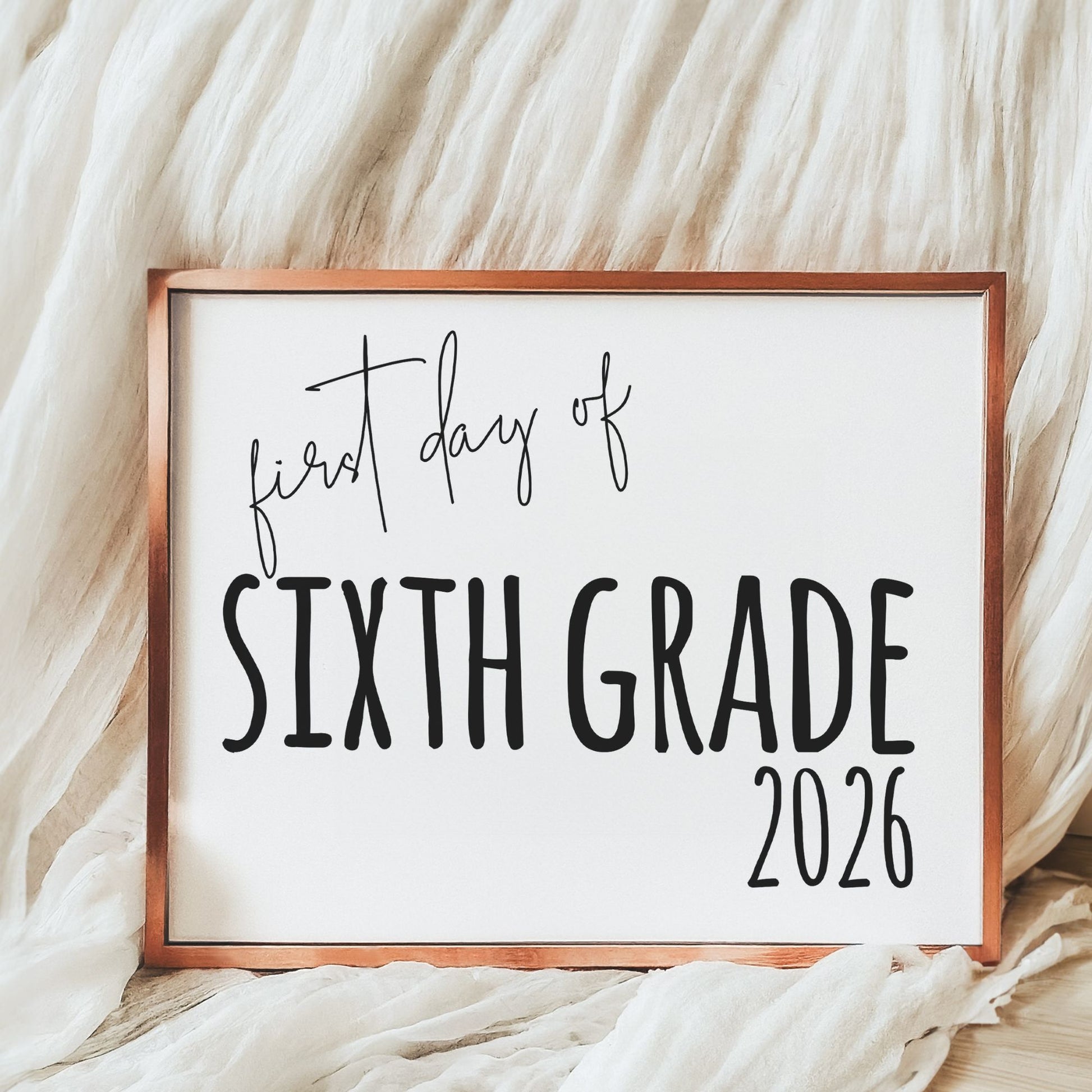 Sign with 'first day of Sixth Grade 2026' text on a white background with wooden frame.