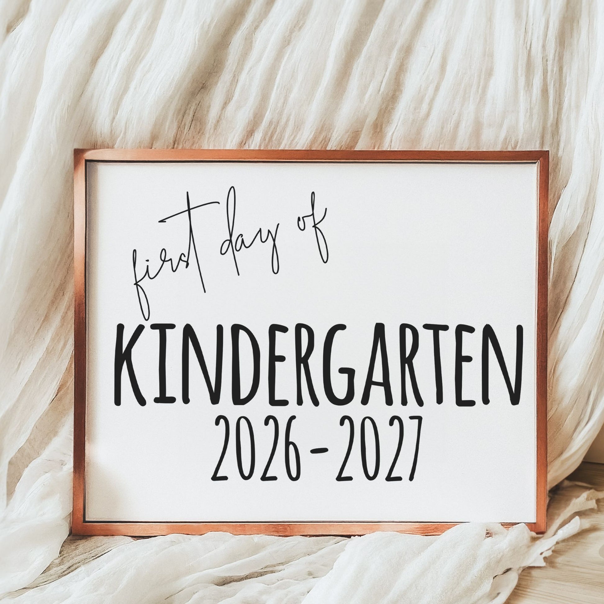 Framed sign with 'first day of Kindergarten 2026-2027' text on a soft fabric background