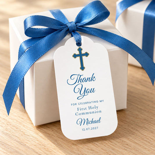A white square gift box tied with a royal blue satin ribbon and bow, with a white hanging tag printed with a blue cross and the words 'Thank You' and 'For celebrating my First Holy Communion Michael 12.07.