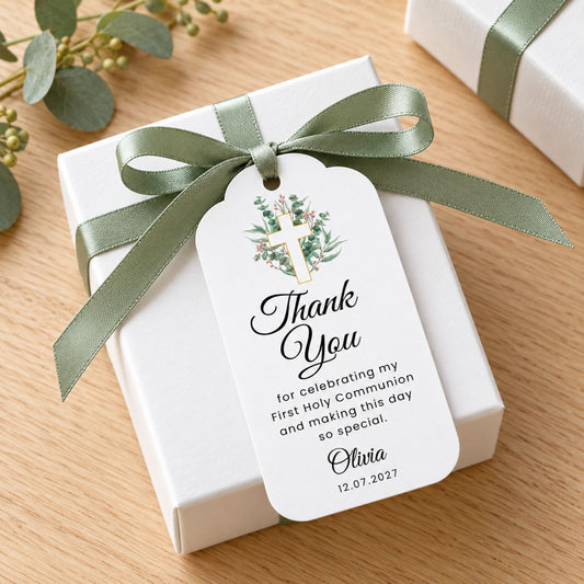 A white gift box tied with an olive green satin ribbon and a personalized thank-you tag featuring a watercolor cross and greenery, placed on a light wood surface.