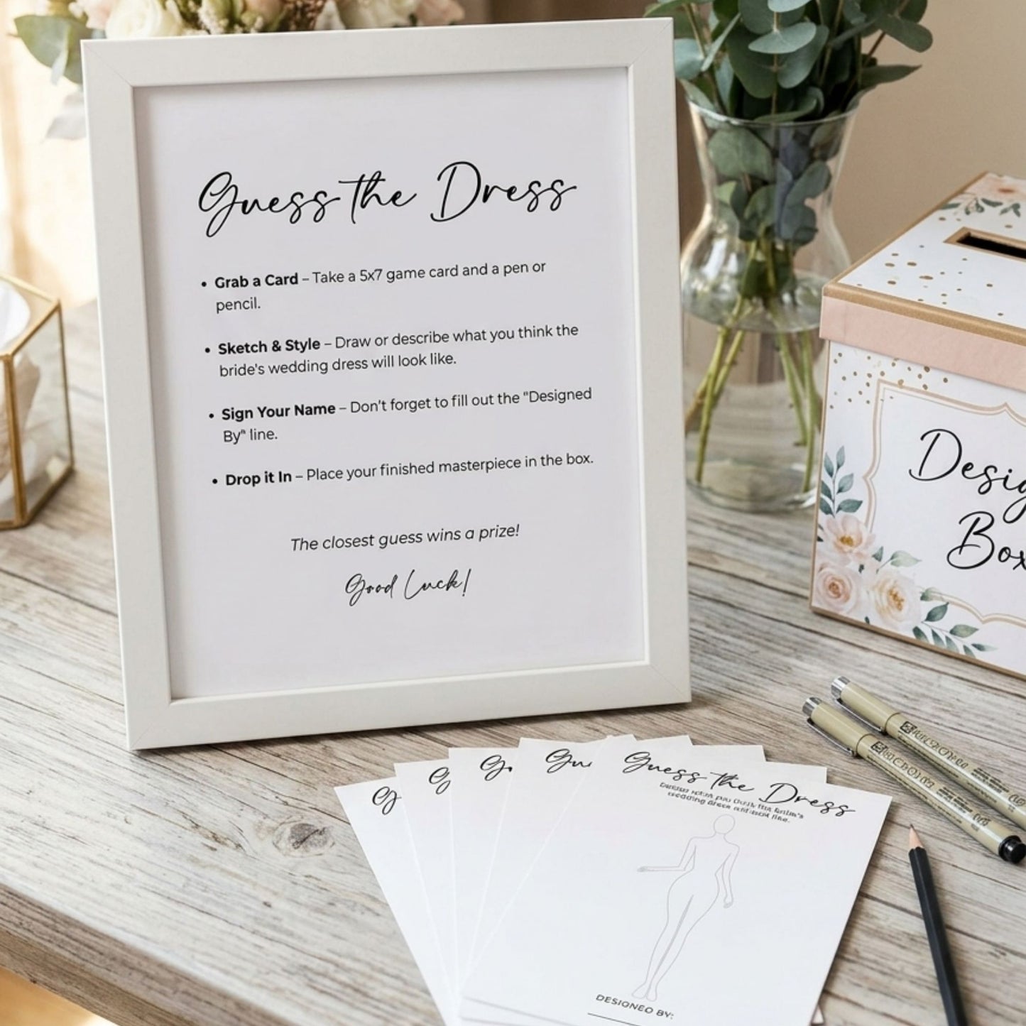 Guess the Dress game set with cards, a frame, and stationery on a wooden surface.