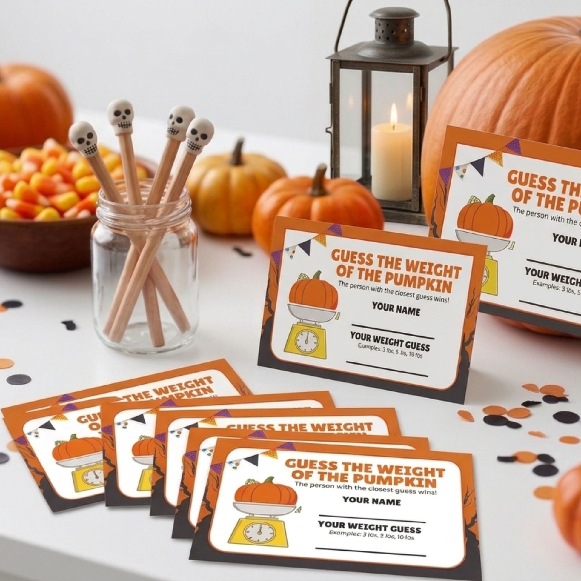 Halloween-themed printable game cards reading 'GUESS THE WEIGHT OF THE PUMPKIN' arranged on a tabletop with pumpkins, candy corn, a lantern, and skull-topped spoons in the background.