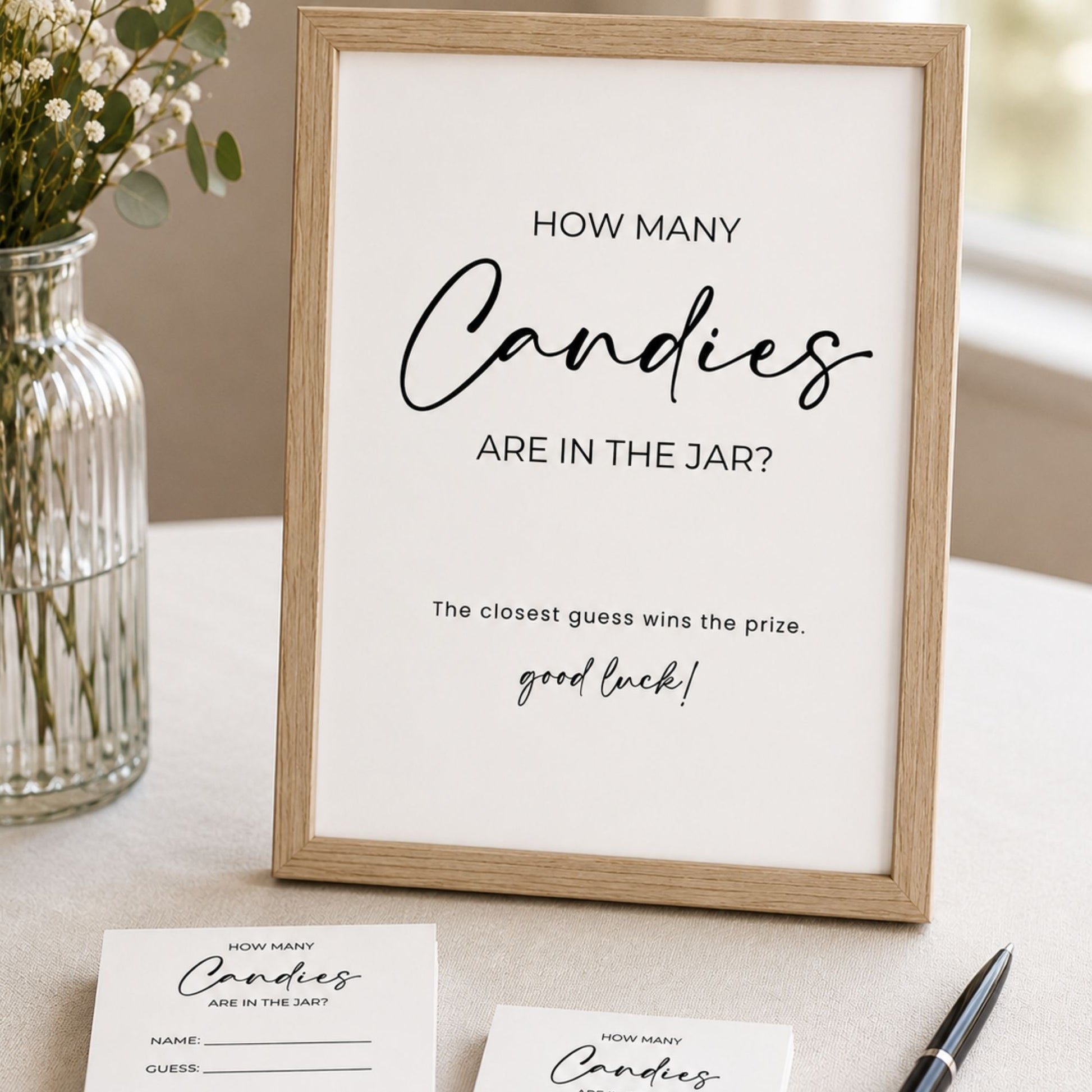 Framed sign with 'How Many Candies Are In The Jar?' game on a table with a vase and pen.