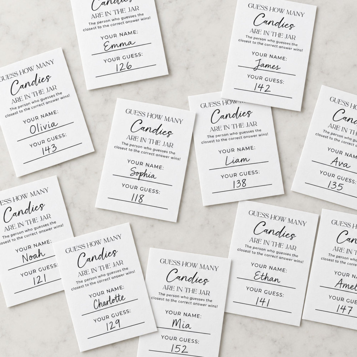 A flat-lay arrangement of personalized candy counting cards on a light marble background. The white cards feature black text and handwritten guesses in blue ink.