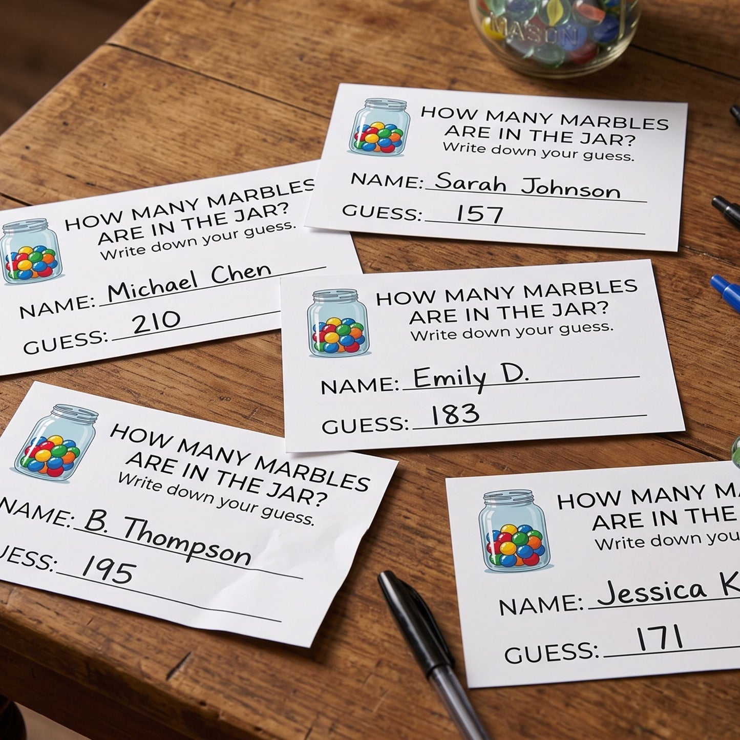 Several printed worksheet cards titled "HOW MANY MARBLES ARE IN THE JAR?" are arranged on a wooden table, each with a small jar illustration and a handwritten name and guess. A glass jar of marbles and pens are also visible in the scene.