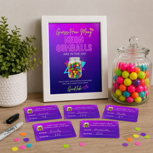 A framed neon gumball guessing game printout stands on a tabletop next to a glass jar filled with colorful gumballs and several purple player cards. The scene is styled with a potted plant, confetti, and a marker on a light wood surface against a beige wall.