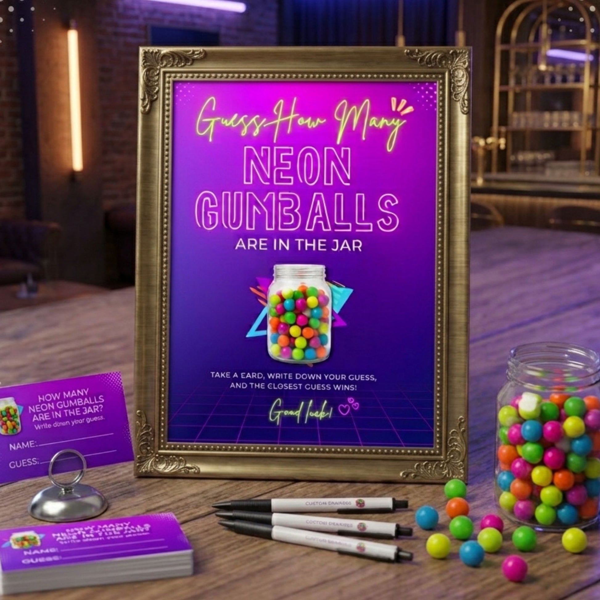 A framed neon-themed candy jar guessing game setup on a wooden table, featuring a purple sign with gold text, a gold frame, a glass jar filled with colorful gumballs, matching gumballs scattered around, cards, pens, and a small stand.