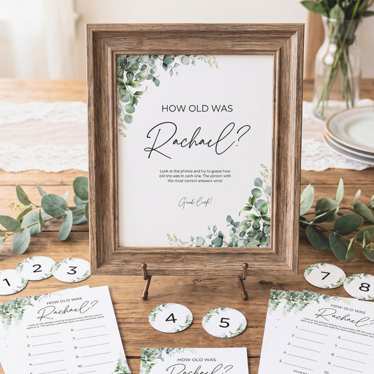 Decorative sign with 'How old was Rachel?' question on a wooden table with eucalyptus leaves.