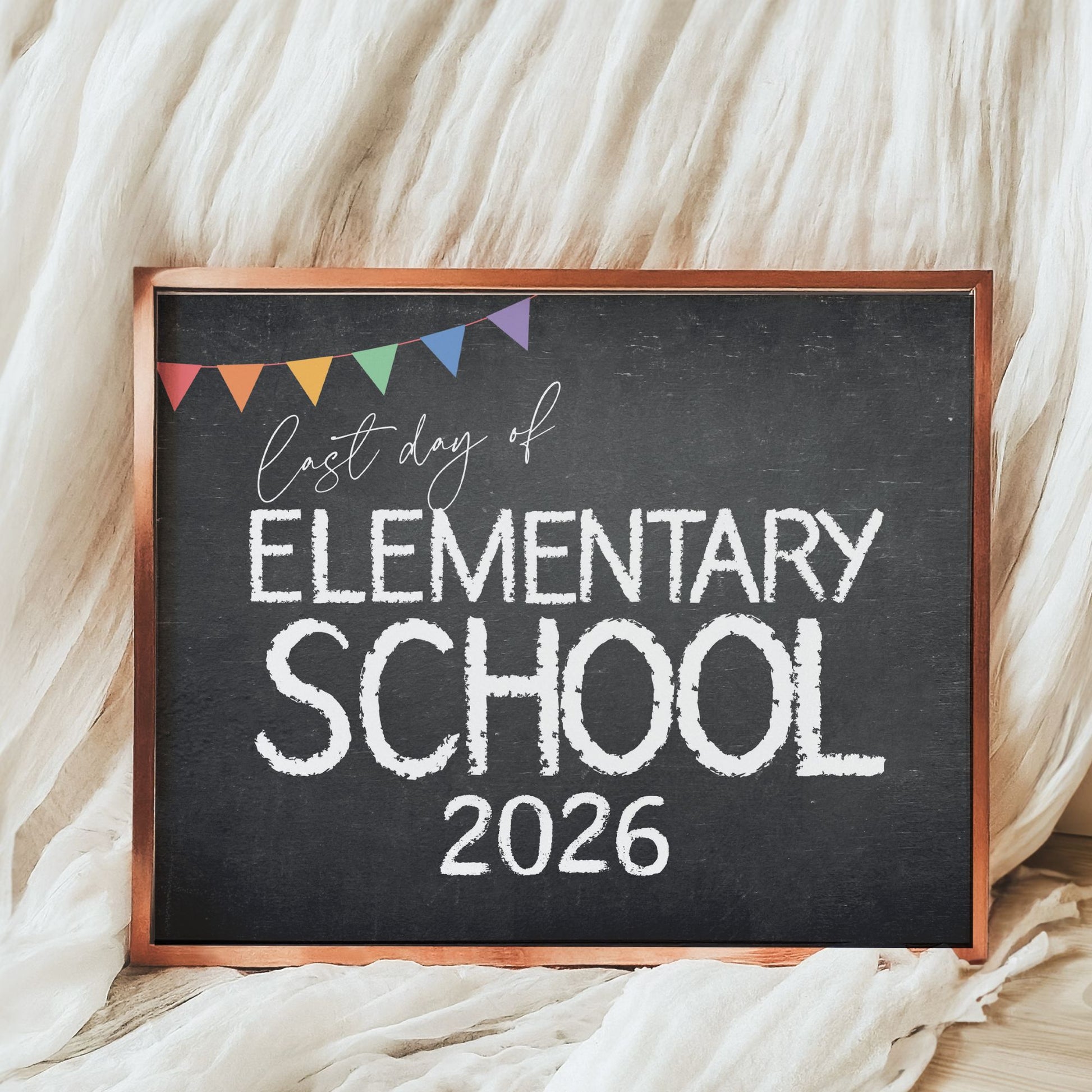 Chalkboard sign with 'Last day of Elementary School 2026' text on a soft white fabric background