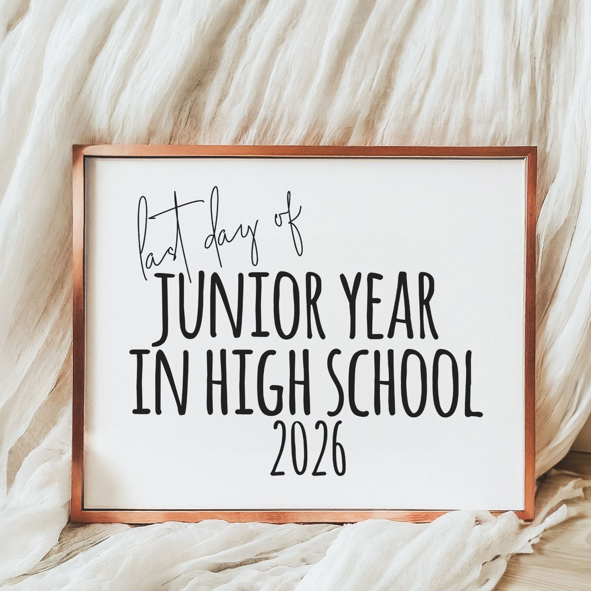 Framed sign with 'last day of junior year in high school 2026' text on a soft fabric background