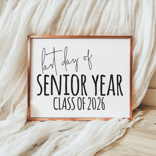 Minimalist last day of senior year class of 2026 printable sign in black and white displayed in a wood frame with neutral fabric backdrop for graduation photos.