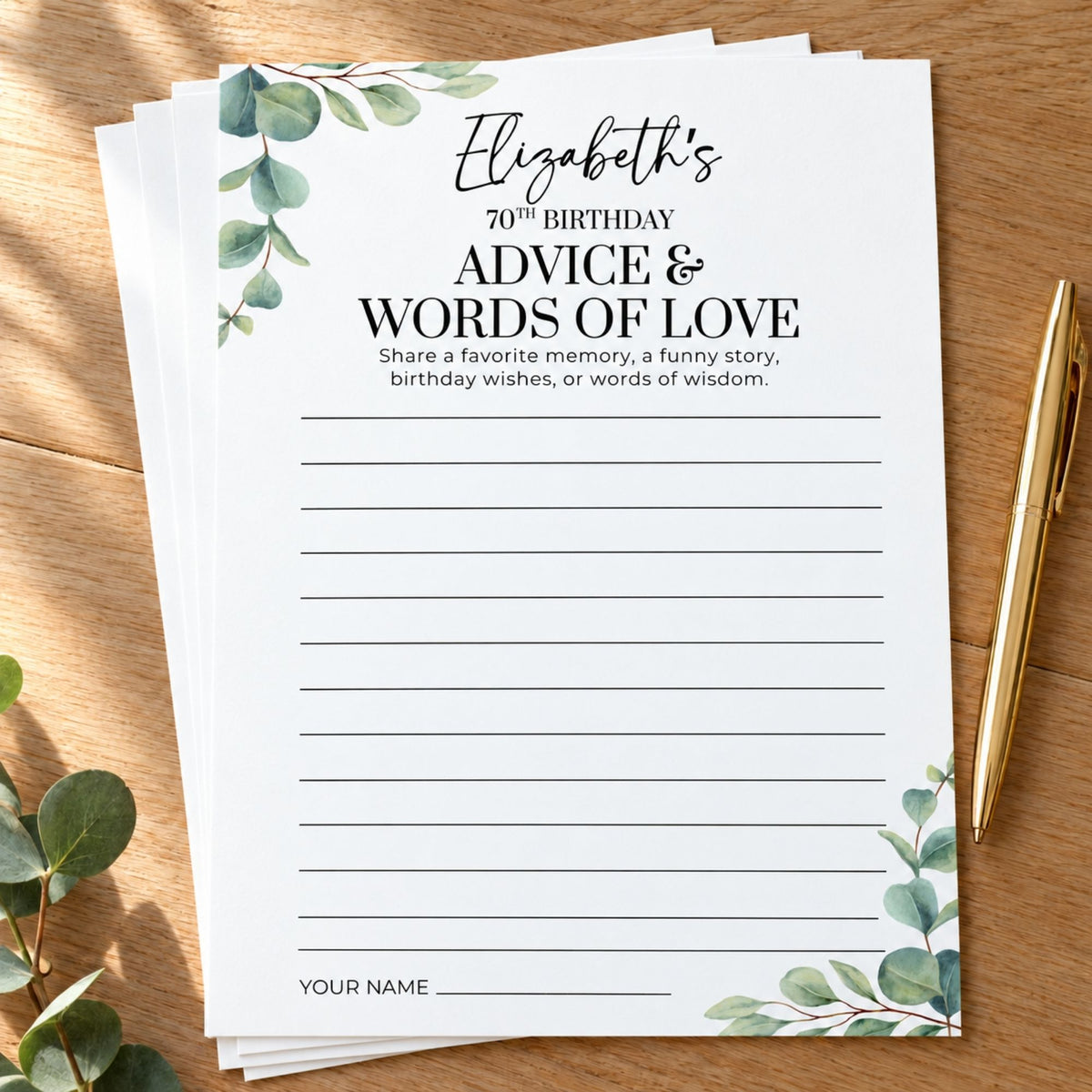 A stack of white custom writing cards with green eucalyptus illustrations in the corners, displayed on a wooden tabletop next to a gold pen.