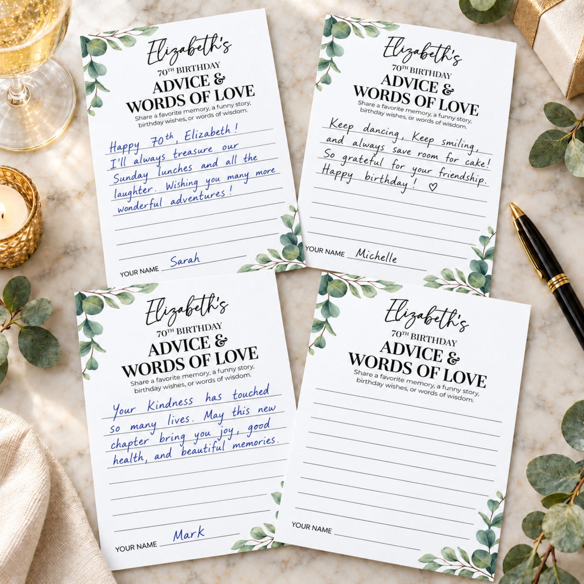 Four personalized birthday cards with green eucalyptus leaf borders, arranged on a beige fabric surface with a gold candle, wrapped gift box, and black pen as props.