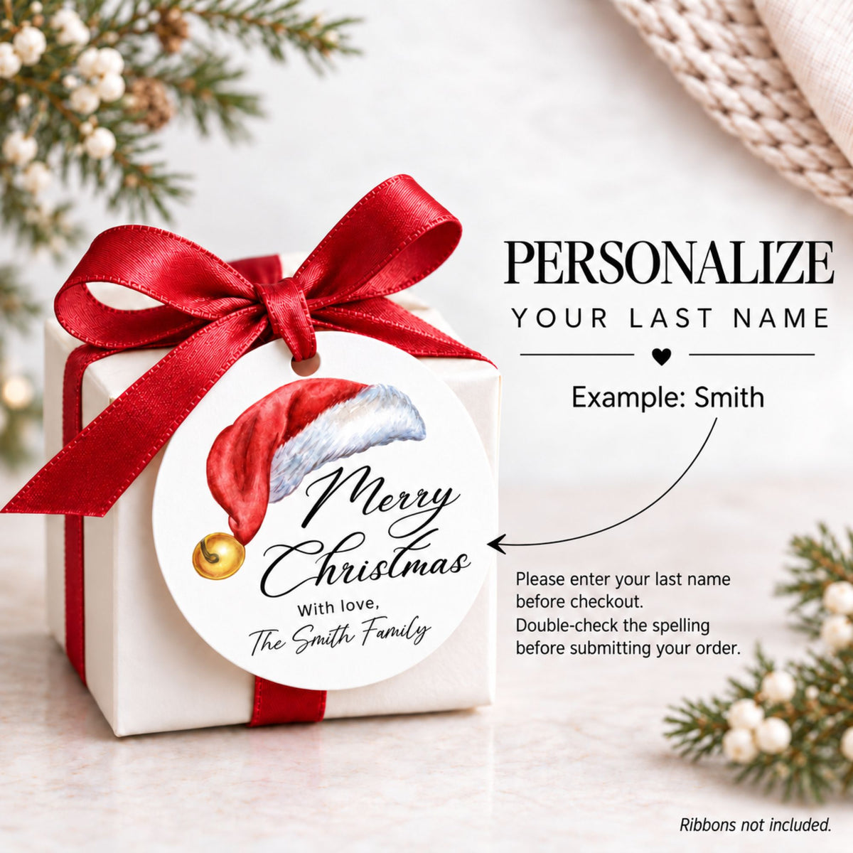 A white gift box tied with a red ribbon and bow, featuring a round printed tag that says Merry Christmas with love, The Smith Family and a Santa hat illustration. The image includes a customization callout reading PERSONALIZE YOUR LAST NAME with an example, on a softly styled holiday background with pine branches.