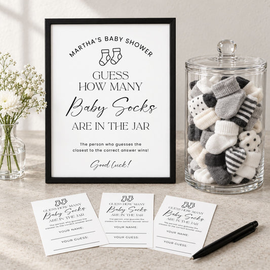 A framed baby shower game sign reading 'Martha's Baby Shower Guess How Many Baby Socks Are in the Jar' is displayed on a tabletop beside a glass jar filled with baby socks, with three matching ticket cards and a pen in front.