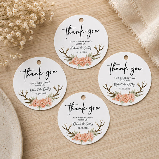 Five round white thank-you tags with floral and antler illustrations, arranged on a light wood surface with dried flowers and fabric props.