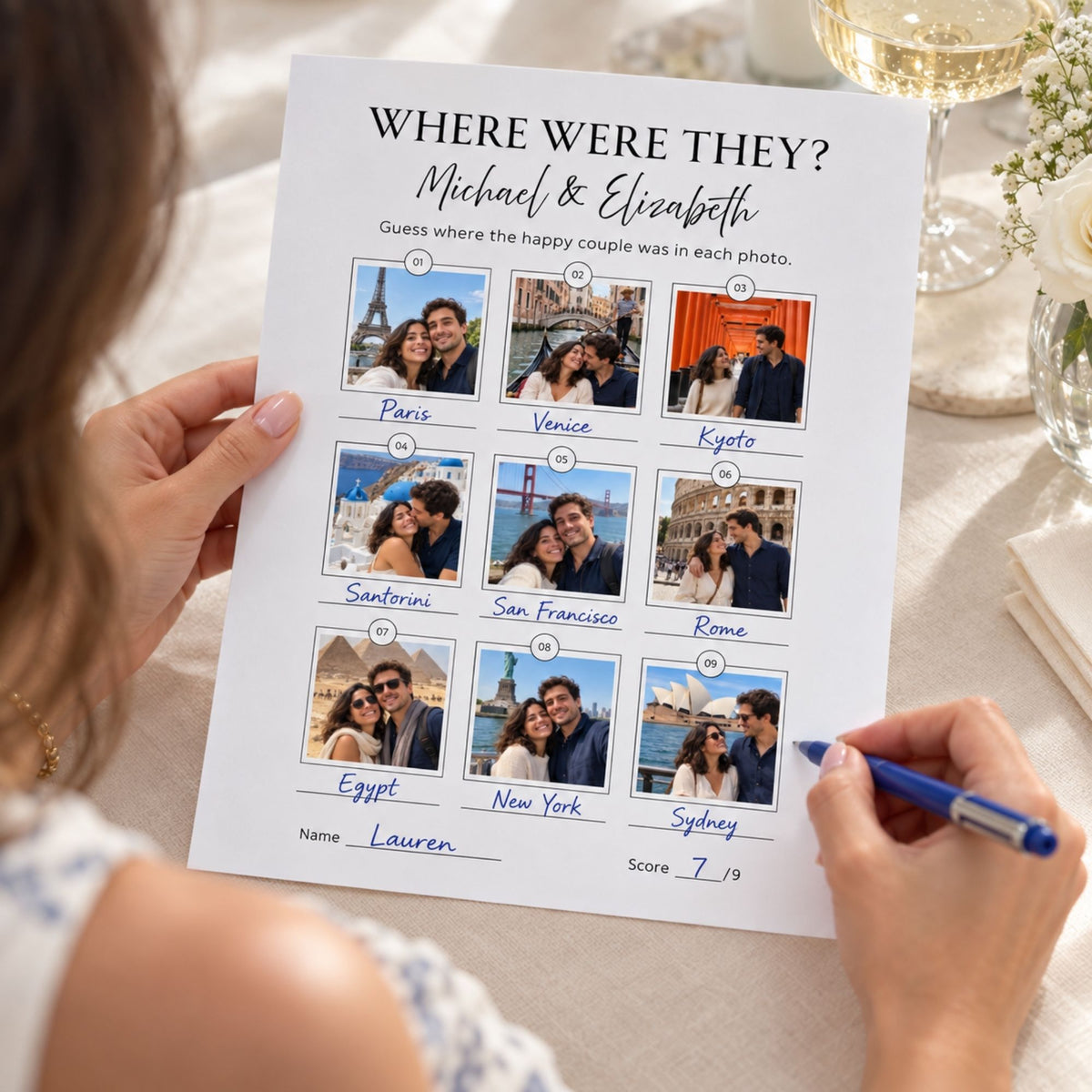 A person holds a printed personalized couple photo guessing worksheet titled "WHERE WERE THEY? Michael & Elizabeth" over a table setting, with photos of a couple and a blue pen in hand.