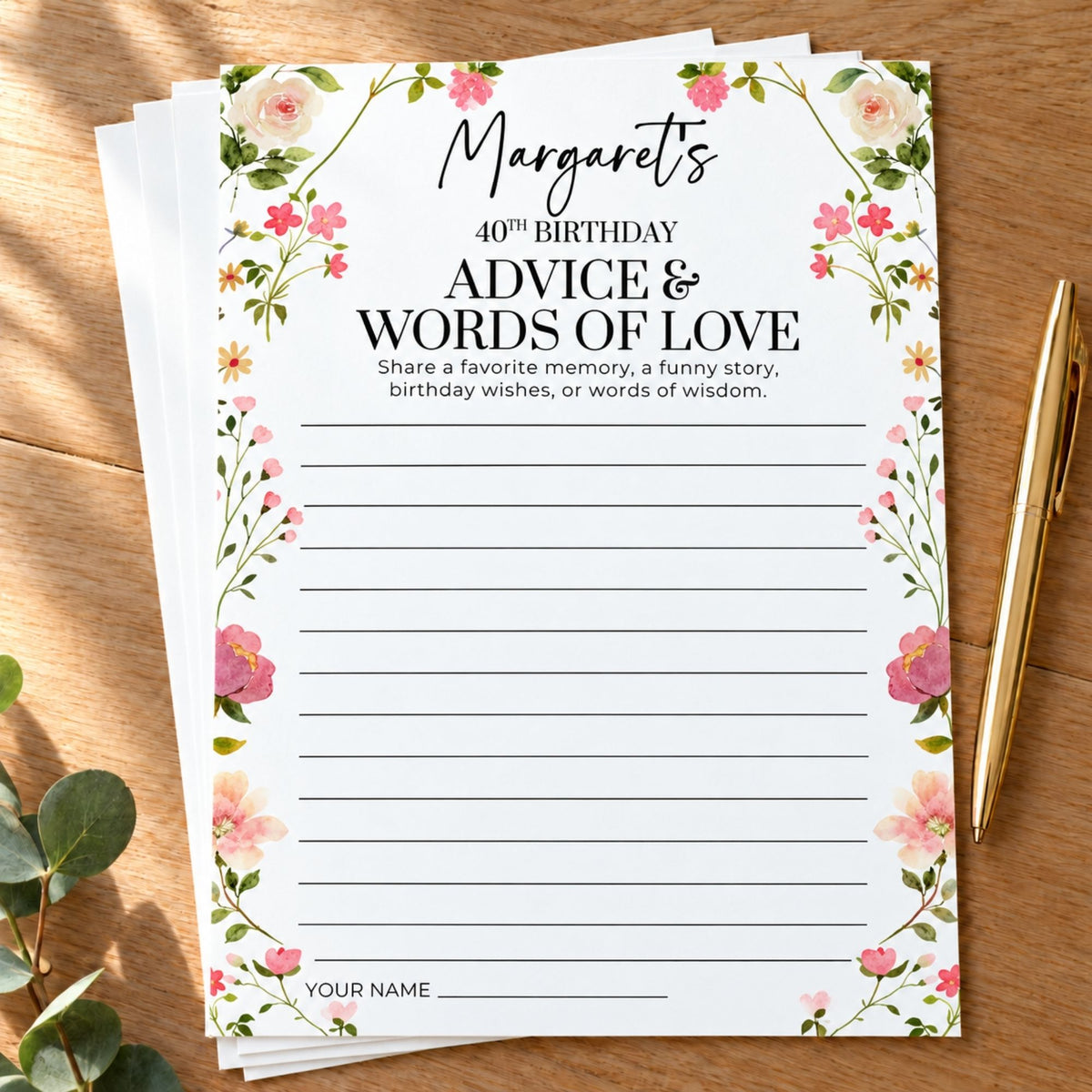 A stack of personalized floral birthday party games on a wooden tabletop, with a gold pen and eucalyptus leaves nearby. The top card reads 'Margaret's 40th Birthday Advice & Words of Love' with lined writing space and a floral border.