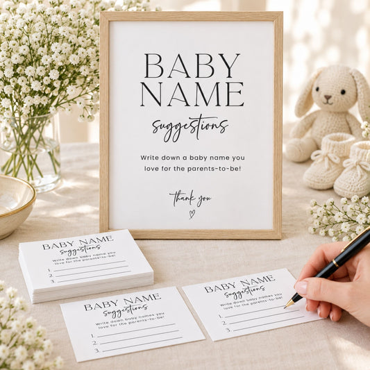 A framed baby name suggestion sign stands on a light fabric surface, with matching printed cards stacked in front and a hand holding a pen over one card. The scene is styled with baby flowers, a knitted bunny toy, and soft natural light.