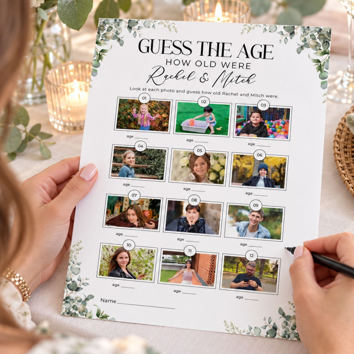 A person holds a printed 'Guess the Age' wedding game sheet with photos of a bride and groom and blank age lines, while another person uses a black pen to fill in answers at a decorated table with candles and greenery.