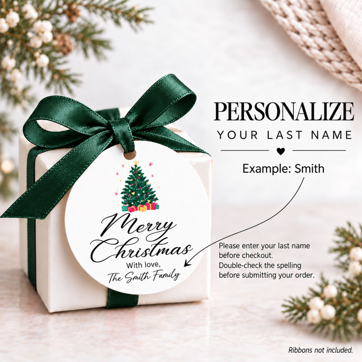 A small white gift box tied with a dark green ribbon and bow, featuring a round printed tag that reads 'Merry Christmas with love, The Smith Family' with a small Christmas tree illustration. The image includes promotional text on the right for personalization, with holiday greenery and a knitted textile in the background.
