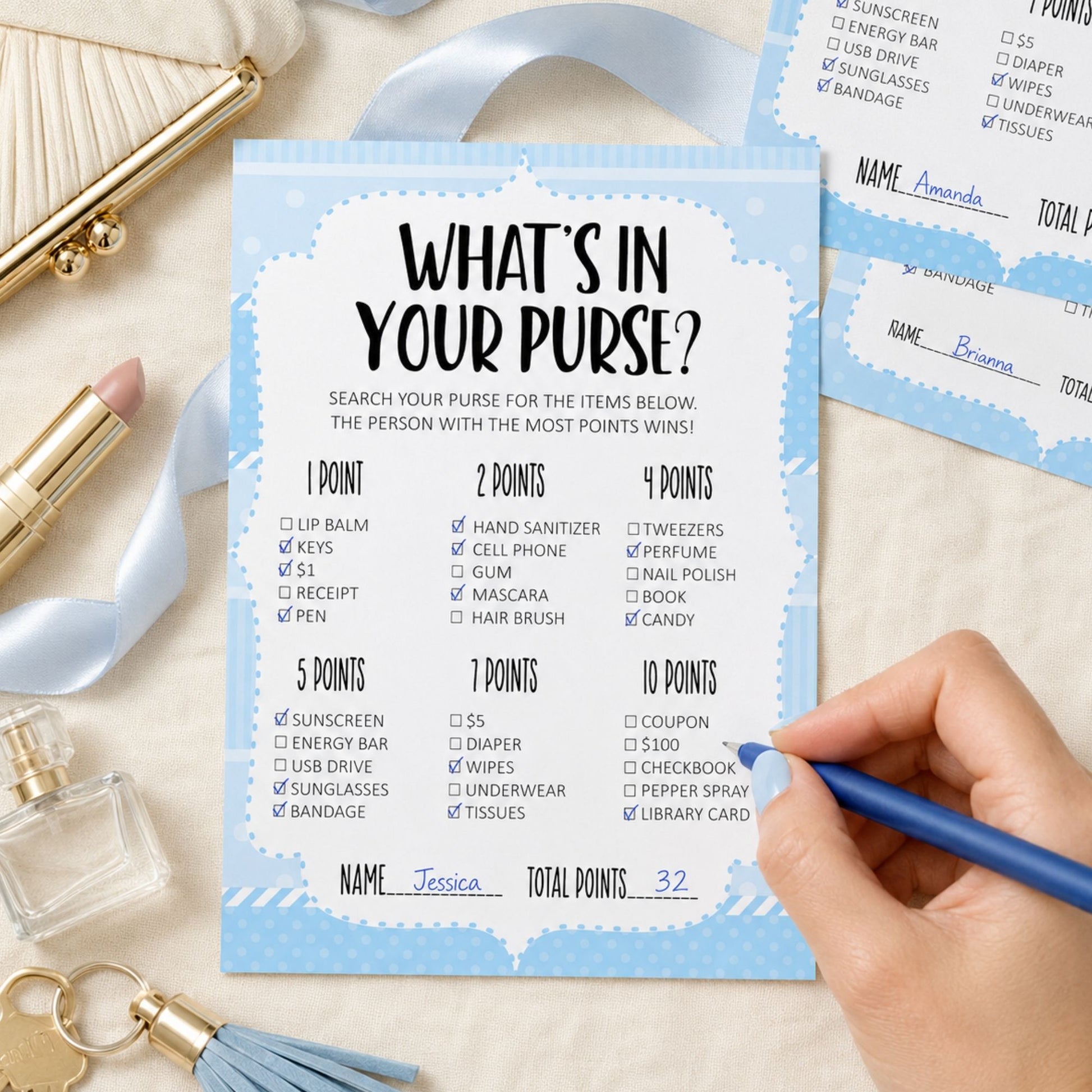 A printed party game card titled "What's in Your Purse?" with blue and white sections listing point values for items like sunscreen, phone, makeup, and candy. A hand is pointing at the card, and other matching cards and gold-toned accessories are visible around it.