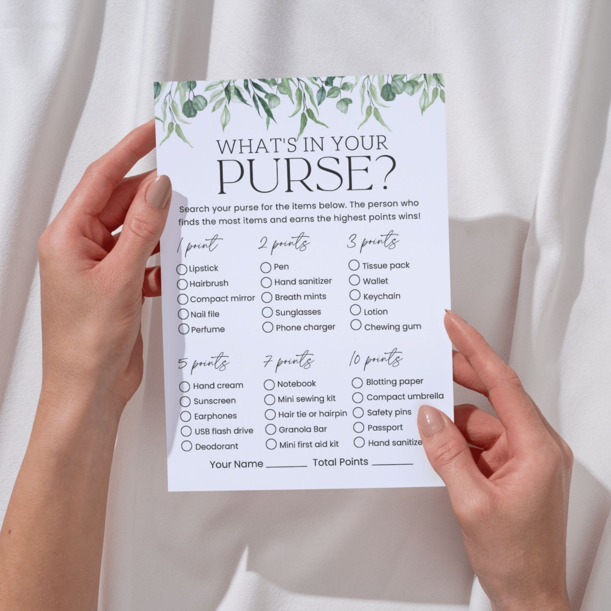 Hand holding a 'What's in Your Purse?' game sheet with greenery design on a white background